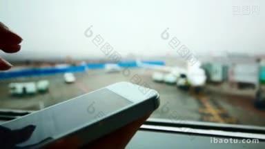 背景是一名女子在机场飞机窗口用智能手机打字的特写镜头